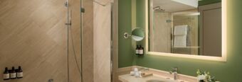 Bathroom interior of Hotel NH Collection Milano Touring with green walls, illuminated mirror, sink, and glass shower enclosure