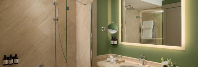 Bathroom interior of Hotel NH Collection Milano Touring with green walls, illuminated mirror, sink, and glass shower enclosure