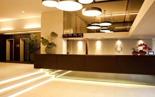 Hotel Manin reception area with modern brown counter, illuminated stairs, hanging circular lights, and digital time display showing world cities