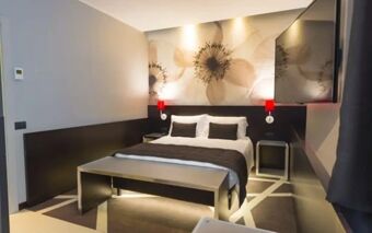 Modern hotel room at Hotel Manin featuring a double bed with cushions, flower artwork, red wall lights, and a mounted TV