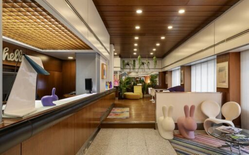 Reception area of Hotel Mediolanum with wooden ceiling, modern furniture including bunny-shaped chairs, and plants hanging above