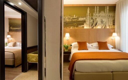Double bedroom at Starhotel Ritz with orange bed runner and cushions, wooden headboard, and cityscape artwork above bed