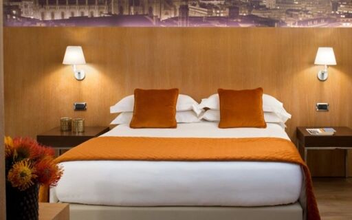 Modern bedroom at Starhotel Ritz with a large bed featuring orange pillows and blanket and two bedside tables with lamps