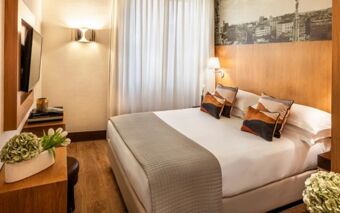 A modern hotel room at Starhotel Ritz featuring a double bed, decorative pillows, wooden wall paneling, and a mounted TV