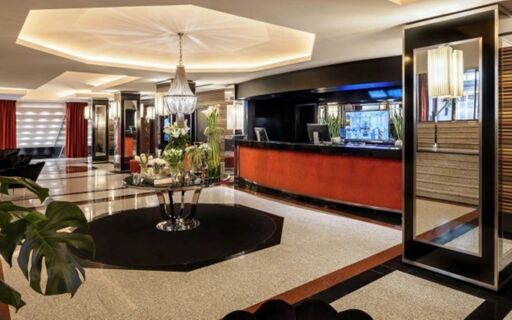 Spacious lobby of Starhotel Ritz with a chandelier, central round table with flowers, and a long red reception desk