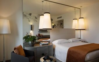 Modern hotel room at Starhotel E.c.h.o with a double bed, hanging lamps, armchair, side tables, and decorative plants