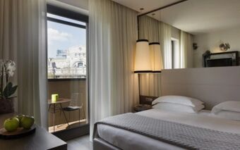 Hotel room at Starhotel E.c.h.o with a double bed, bedside lamps, balcony with table and chair, and city view visible outside