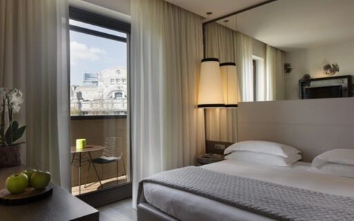 Hotel room at Starhotel E.c.h.o with a double bed, bedside lamps, balcony with table and chair, and city view visible outside