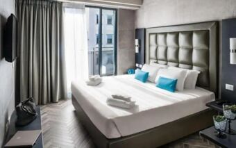 King size bed with white linens and blue pillows in a modern room at Spice Hotel Milano with a wall-mounted TV and balcony windows
