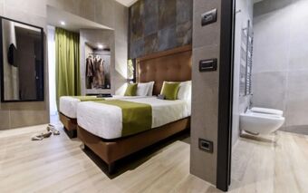 A modern hotel room at Just Hotel Milano with two single beds, green accents, a walk-in closet, and an adjacent bathroom