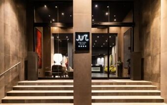Entrance of Just Hotel Milano featuring wide stairs leading to glass doors framed by stone walls and illuminated signage