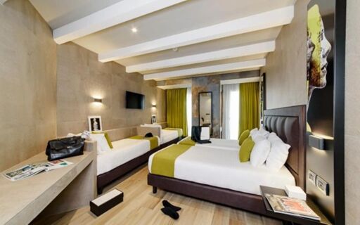 Spacious hotel room at Just Hotel Milano with one double bed, one single bed, desk, wall-mounted TV, and decorative wall art