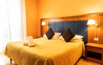 King-size bed with yellow bedspread, two black pillows, wooden headboard, nightstands with lamps in Hotel Berlino room