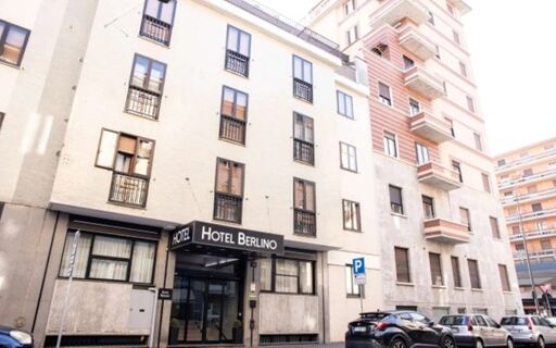 Hotel Berlino exterior with multiple windows, entrance canopy, parked cars, and adjacent apartment buildings visible