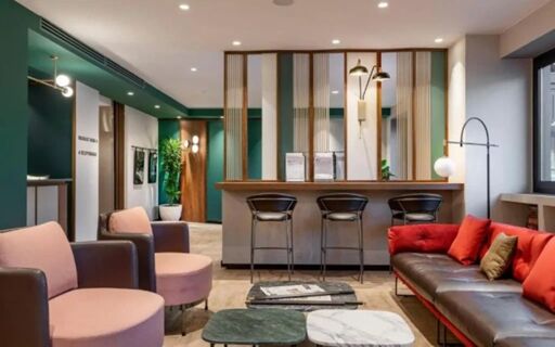 Contemporary lounge area at Hotel Canada with pink and brown chairs, marble coffee tables, a bar with stools, and red pillows on a brown sofa