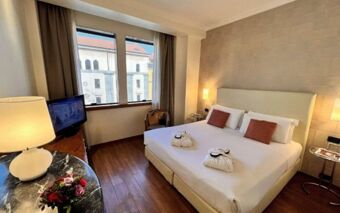 Hotel room at Best Western Hotel City featuring a double bed with pillows, a television, a round table with a lamp and flowers, and a large window