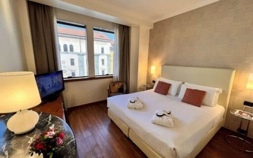 Hotel room at Best Western Hotel City featuring a double bed with pillows, a television, a round table with a lamp and flowers, and a large window