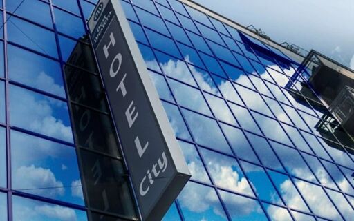 Reflective glass windows showing clouds and sky on the exterior of Best Western Hotel City with a vertical hotel sign visible