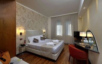 Hotel room at Best Western Hotel City with a double bed, bedside lamps, patterned wallpaper, TV, wooden floor, and a red chair