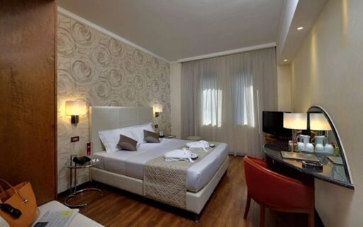 Hotel room at Best Western Hotel City with a double bed, bedside lamps, patterned wallpaper, TV, wooden floor, and a red chair