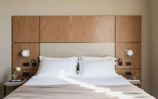 A modern hotel room bed with white pillows and sheets, beige blanket, wooden headboard, and bedside tables at Hotel Cristoforo Colombo
