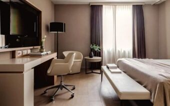 Hotel Cristoforo Colombo room featuring a flat-screen TV, desk with chair, floor lamp, bed with bench, and a large window with curtains
