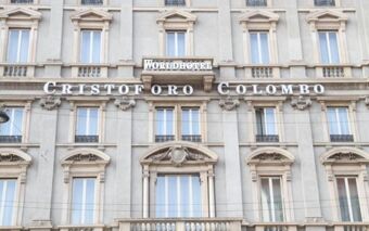 Facade of a stone building displaying large letters and a sign for Hotel Cristoforo Colombo and Worldhotel above several windows