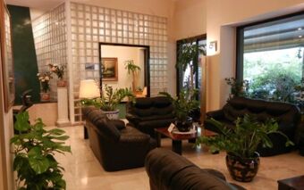 A seating area with black leather sofas and various potted plants in the lobby of Hotel Delle Nazioni