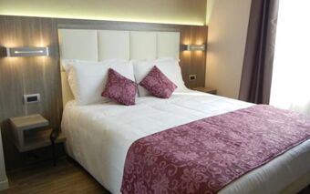 Double bed with white linens, two purple patterned pillows and runner, bedside tables, and lights in Hotel Delle Nazioni room