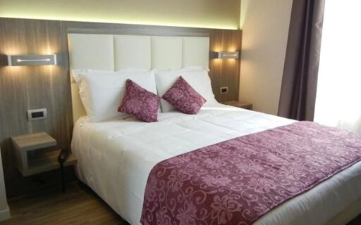 Double bed with white linens, two purple patterned pillows and runner, bedside tables, and lights in Hotel Delle Nazioni room