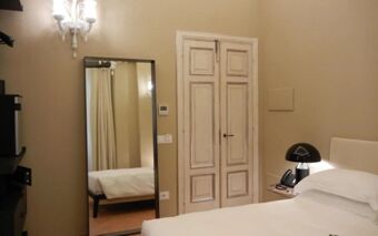 Hotel Delle Nazioni room featuring a white bed, bedside table with black lamp and phone, tall mirror, and double panel door