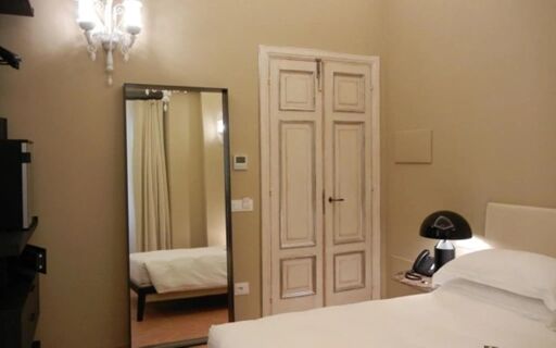 Hotel Delle Nazioni room featuring a white bed, bedside table with black lamp and phone, tall mirror, and double panel door