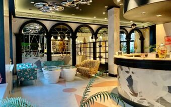 Lobby area of Casual Eclettico Milano Hotel featuring a black curved reception desk, floral armchairs, large mirrors, and modern ceiling lights