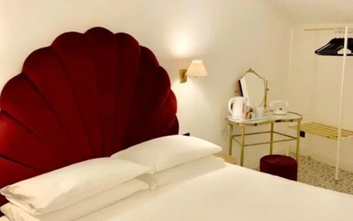 A hotel room at Casual Eclettico Milano Hotel with a large red shell-shaped headboard, white bedding, and a small table with a kettle and telephone