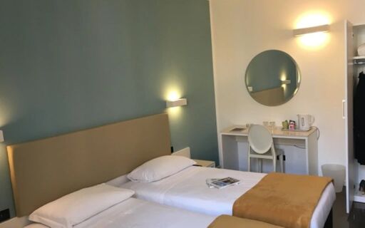 Twin beds with white linens and mustard throws in a hotel room featuring a desk, chair, round mirror at Casual Eclettico Milano Hotel