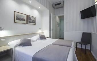 Two single beds with white linens and gray runners in a minimalistic room at Hotel Flora with a wall-mounted TV and chair