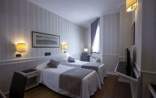 Hotel Flora room with two single beds, gray bed runners, gray pillows, wooden floor, desk, and wall-mounted TV