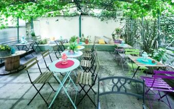 Outdoor seating area at Ostello Bello Grande Hostel with colorful metal tables, wooden chairs, and green plants