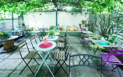 Outdoor seating area at Ostello Bello Grande Hostel with colorful metal tables, wooden chairs, and green plants