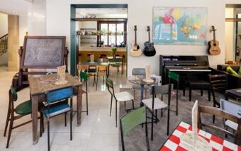 Seating area with tables, chairs, guitars on the wall, a piano, and a welcome sign at Ostello Bello Grande Hostel