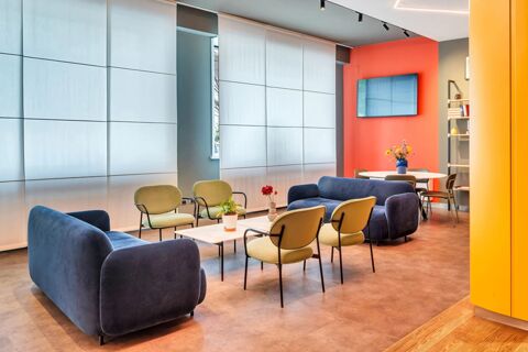 Modern lounge area with blue sofas, green chairs, a white table with plants, and a wall-mounted TV at B&B Hotel Milano Aosta