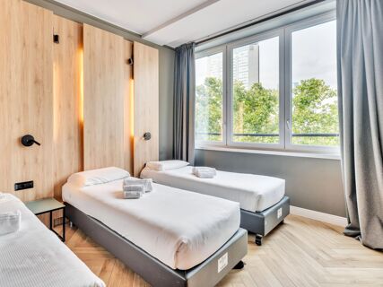Two single beds with white linens and folded towels in a room with wooden panels and large windows at B&B Hotel Milano Aosta