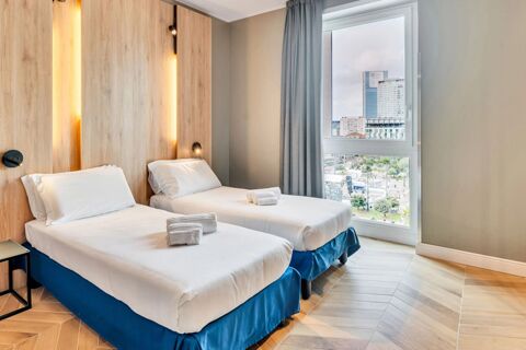 Two single beds with white linens and towels near a large window with a city view inside B&B Hotel Milano Aosta