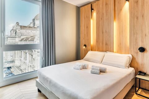Bright hotel room at B&B Hotel Milano Aosta with a neatly made double bed, wooden headboard, and large window view of buildings