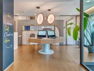 Reception area with self check-in kiosks, modern lighting, welcome sign, and green plants at B&B Hotel Milano Portello