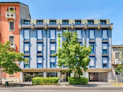 The front facade of B&B Hotel Milano Portello with blue window frames, closed shutters, green trees, and clear blue sky above