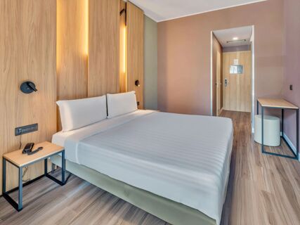 King-size bed with white bedding and pillows against a wooden wall with vertical lights in B&B Hotel Milano Portello room