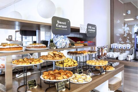 Various baked goods including croissants, muffins, and cakes displayed on wooden shelves in B&B Hotel Milano Portello