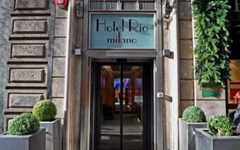 Entrance of Hotel Rio Milano with glass doors framed by stone walls and four square planters with round green bushes