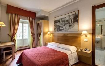 A neatly made double bed with a red quilt in a Hotel Rio room featuring wooden furniture and framed wall art above the headboard